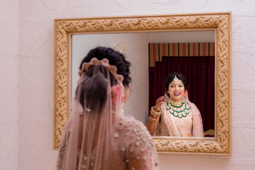 Bride adjusts her jewelry while looking into an ornate framed mirror