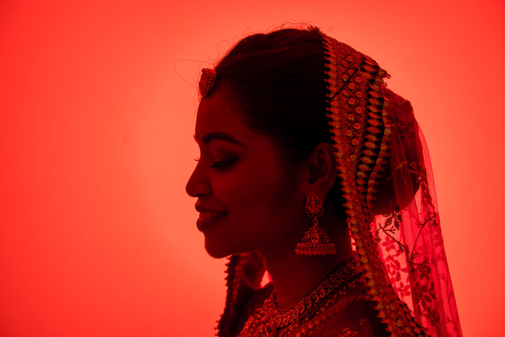 Bride shown in silhouette profile lit by dramatic red light wearing a veil
