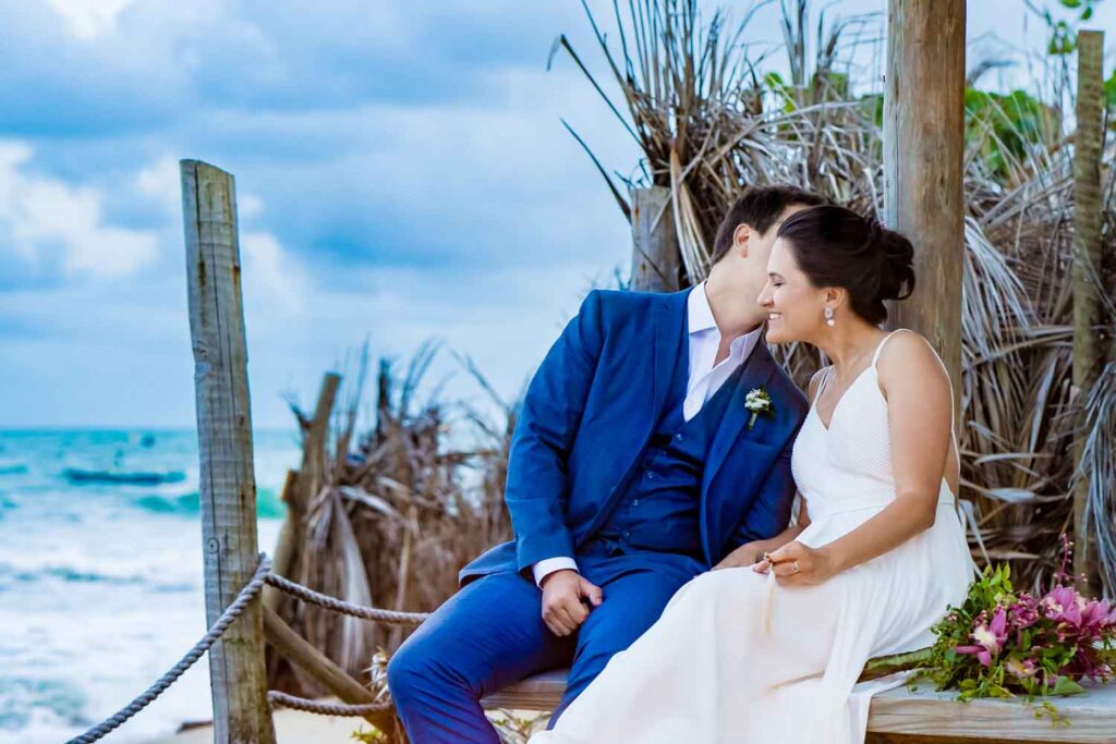 Couple kisses on a wooden beach deck beside ocean waves