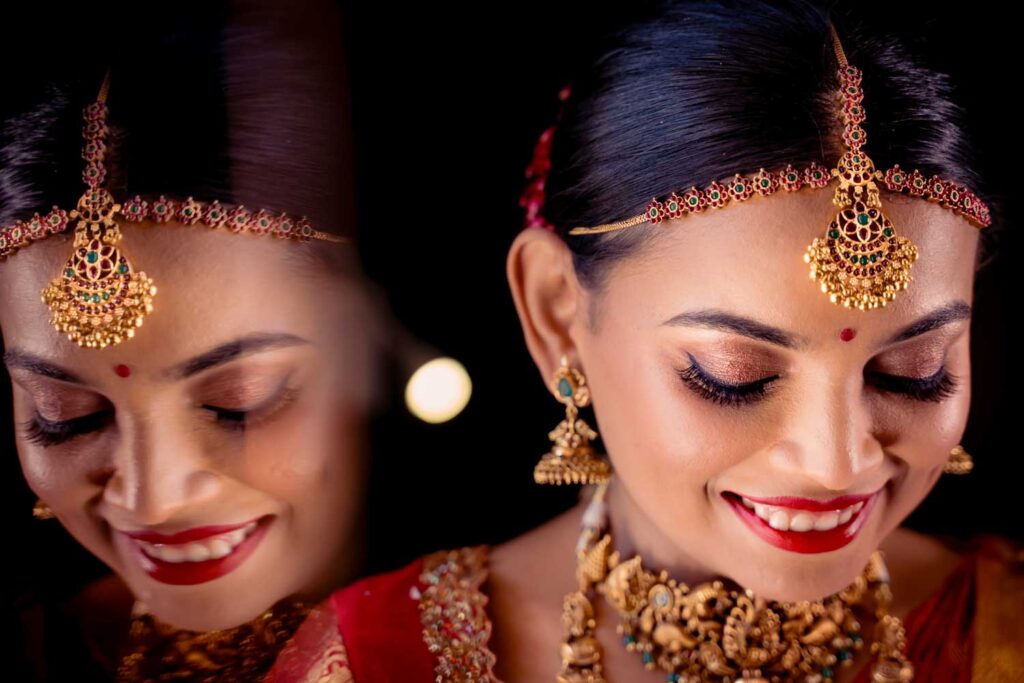Bride smiles in gold jewelry and a red lehenga shown in a mirrored double portrait