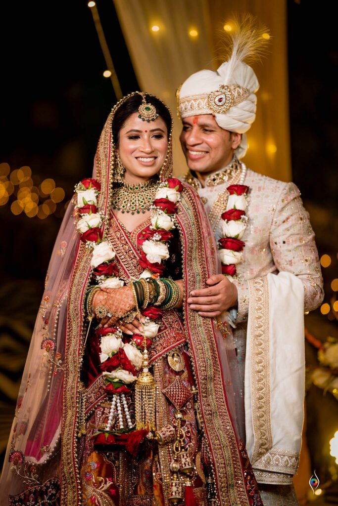 Bride and groom pose together wearing floral garlands under string lights