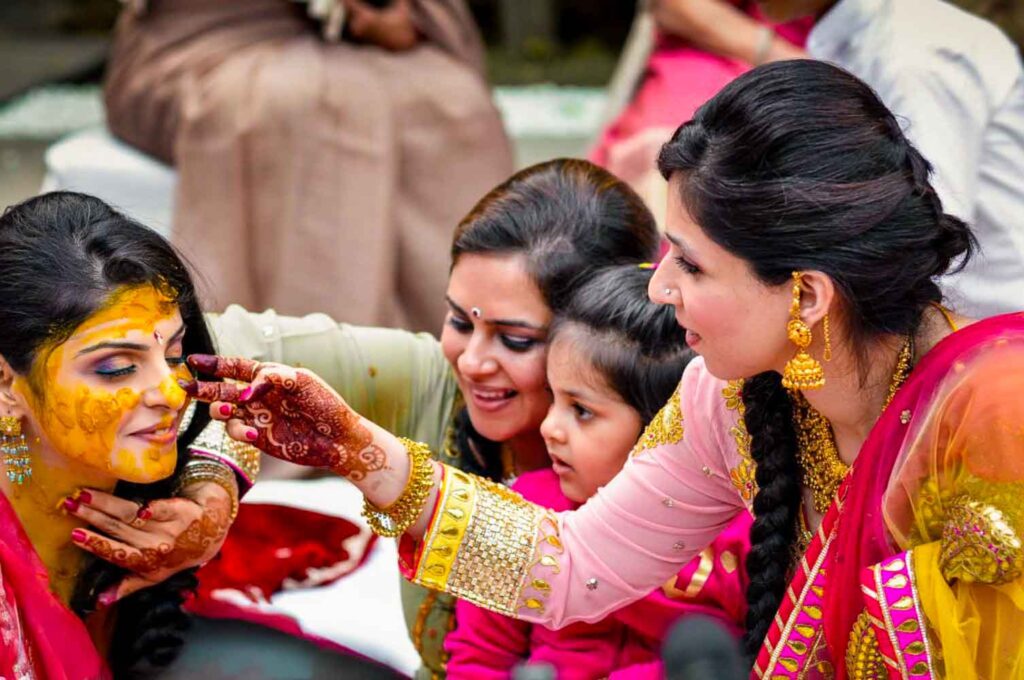 Women apply turmeric haldi paste to the bride while a child watches