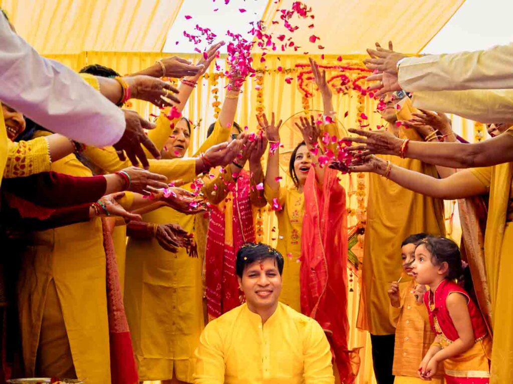Guests in yellow toss flower petals over the groom during his haldi ceremony