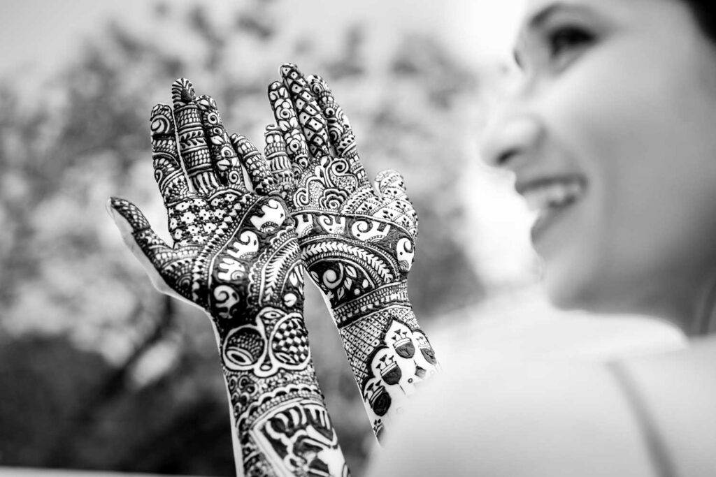 Black and white photo of a raised henna hand with the bride smiling behind