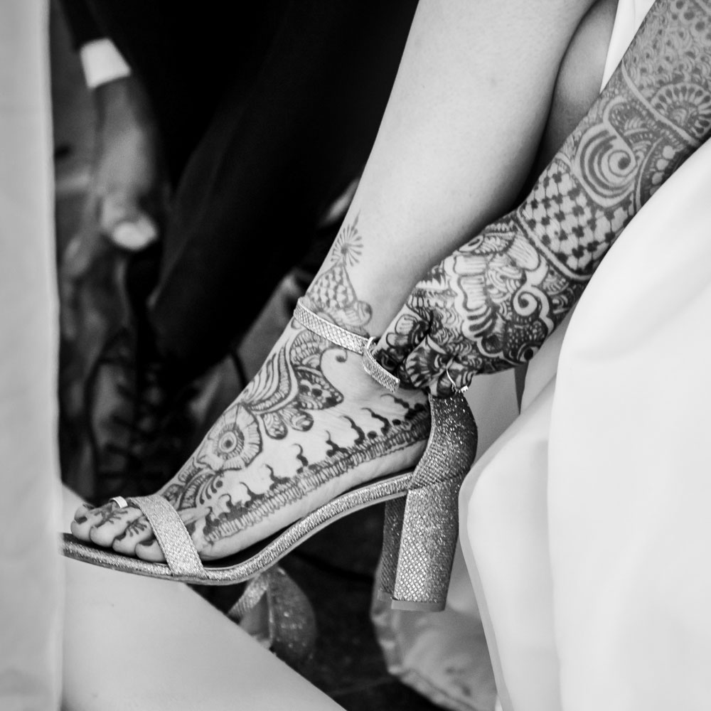 Black and white closeup of henna patterns on a hand and heeled shoe