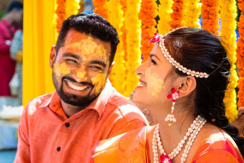 Bride and groom laugh together with turmeric paste on their faces at haldi