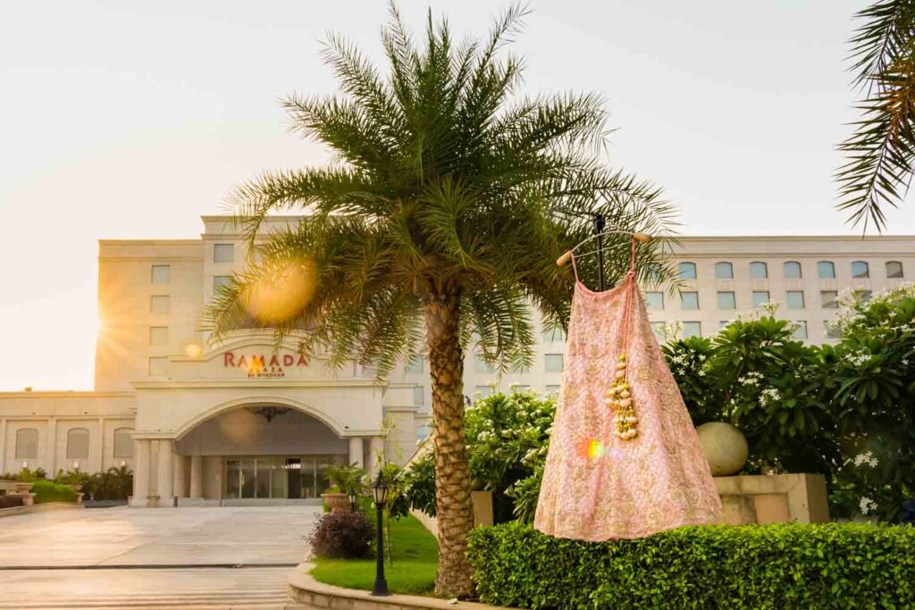 Pink bridal lehenga hangs outdoors near a resort entrance with palm trees