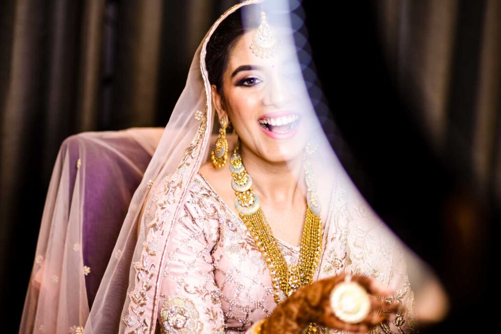 Bride smiles softly behind a sheer veil wearing gold jewelry