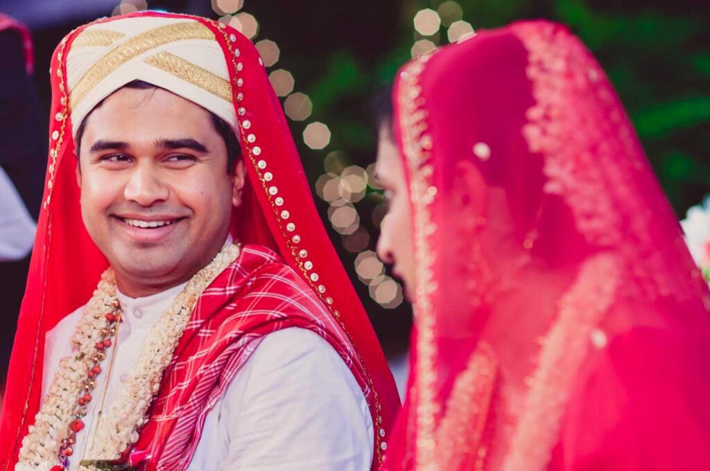 South Indian groom in a red turban smiles beside the veiled bride