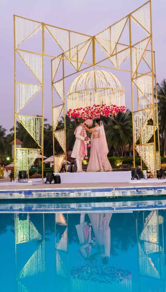 Couple stands under a gold floral installation beside a pool at dusk