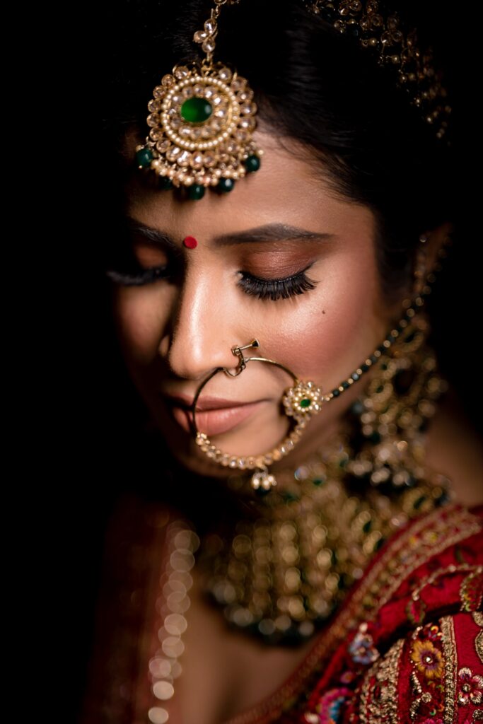 Bride portrait in low light with an emerald maang tikka and red lehenga