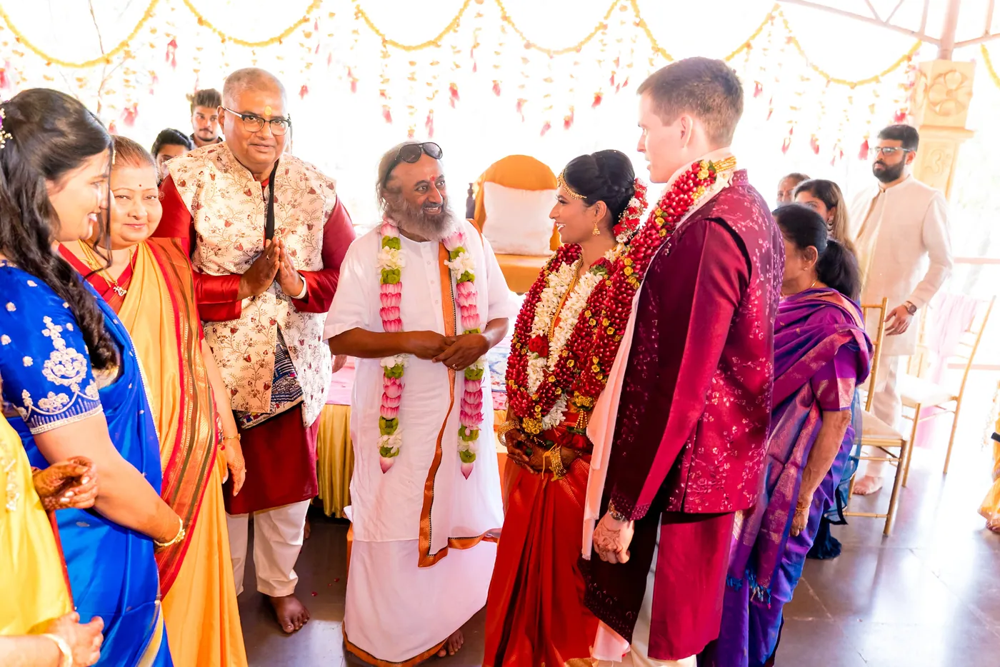 Medha and Stefan stand with Sri Sri Ravi Shankar surrounded by family with folded hands
