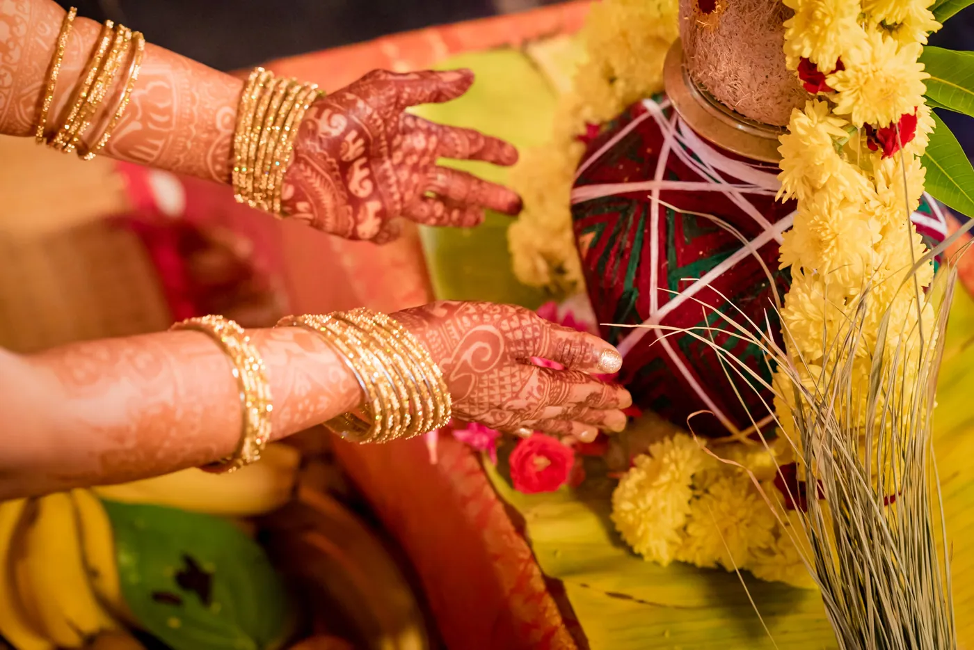 Medha's henna-covered hands arrange a pot with flowers and mango leaves