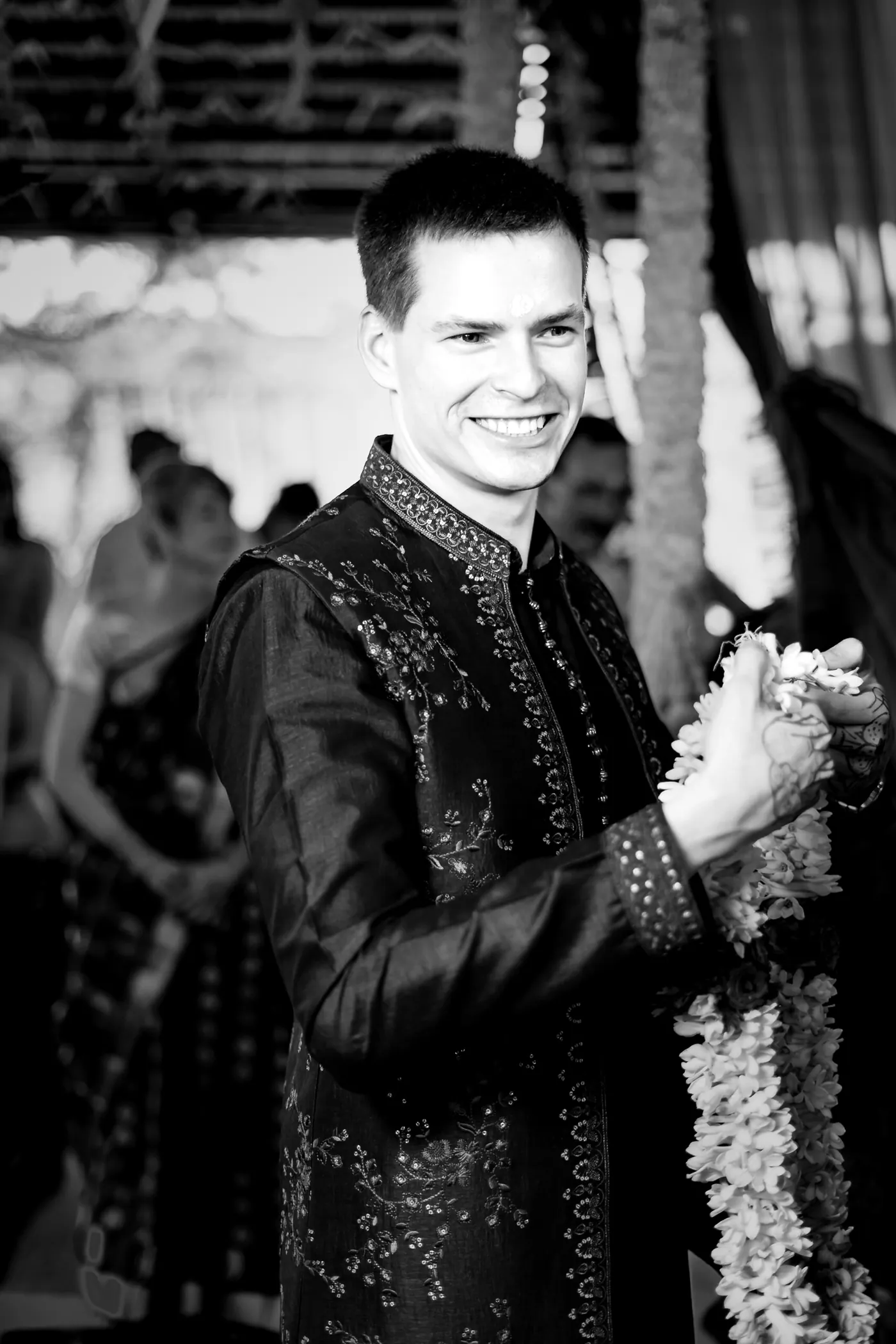 Black and white of Stefan smiling as he holds white flower garlands