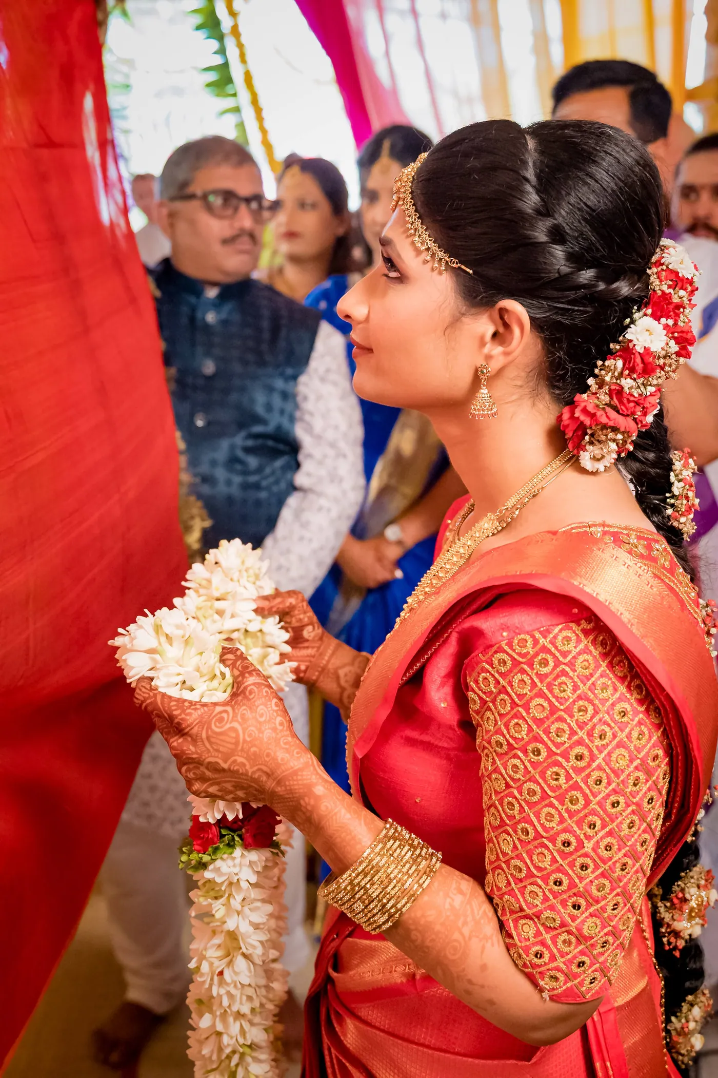 Medha looks up toward Stefan while holding flowers and a jasmine garland
