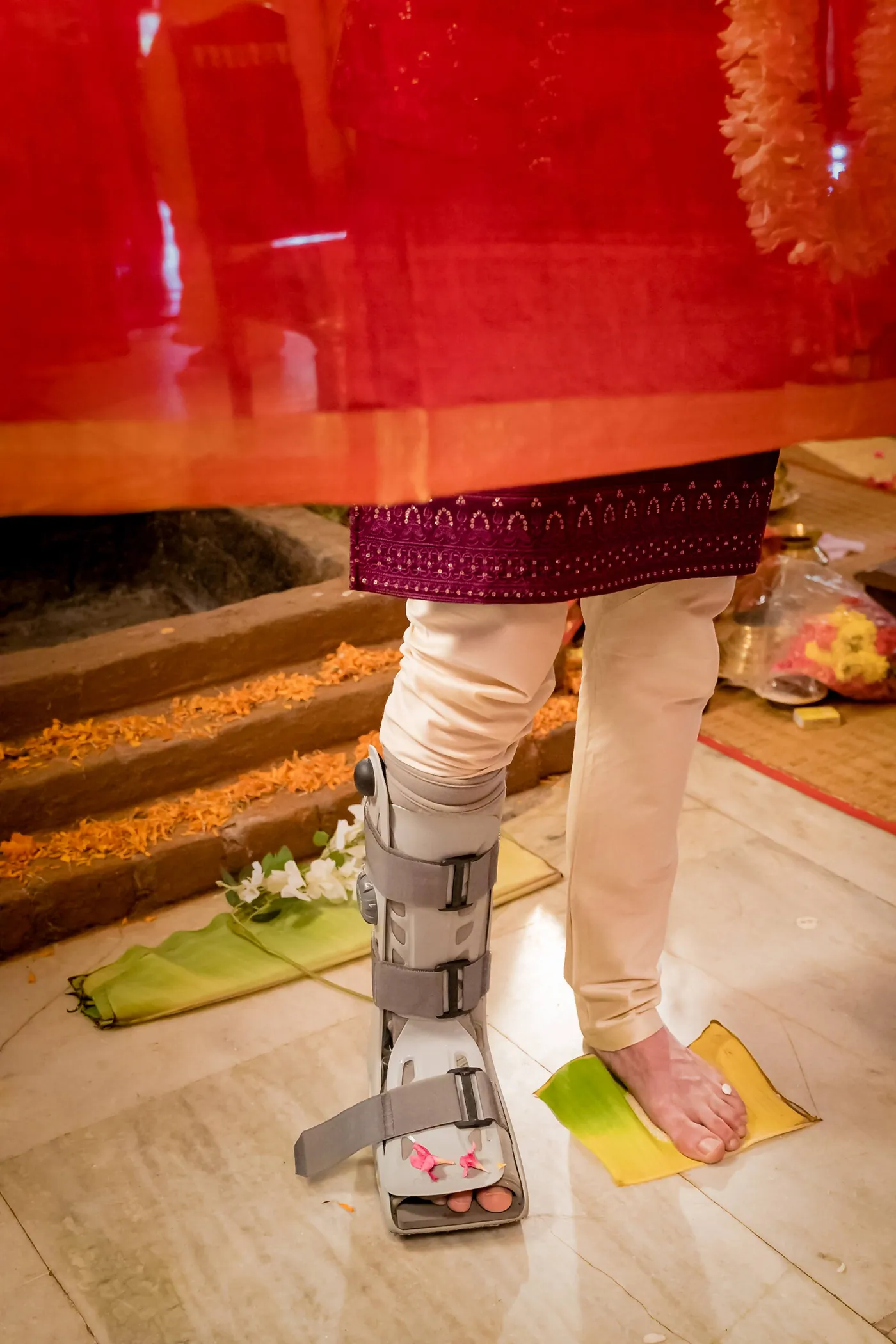 Stefan stands on banana leaves in a walking boot as the red cloth hangs before him