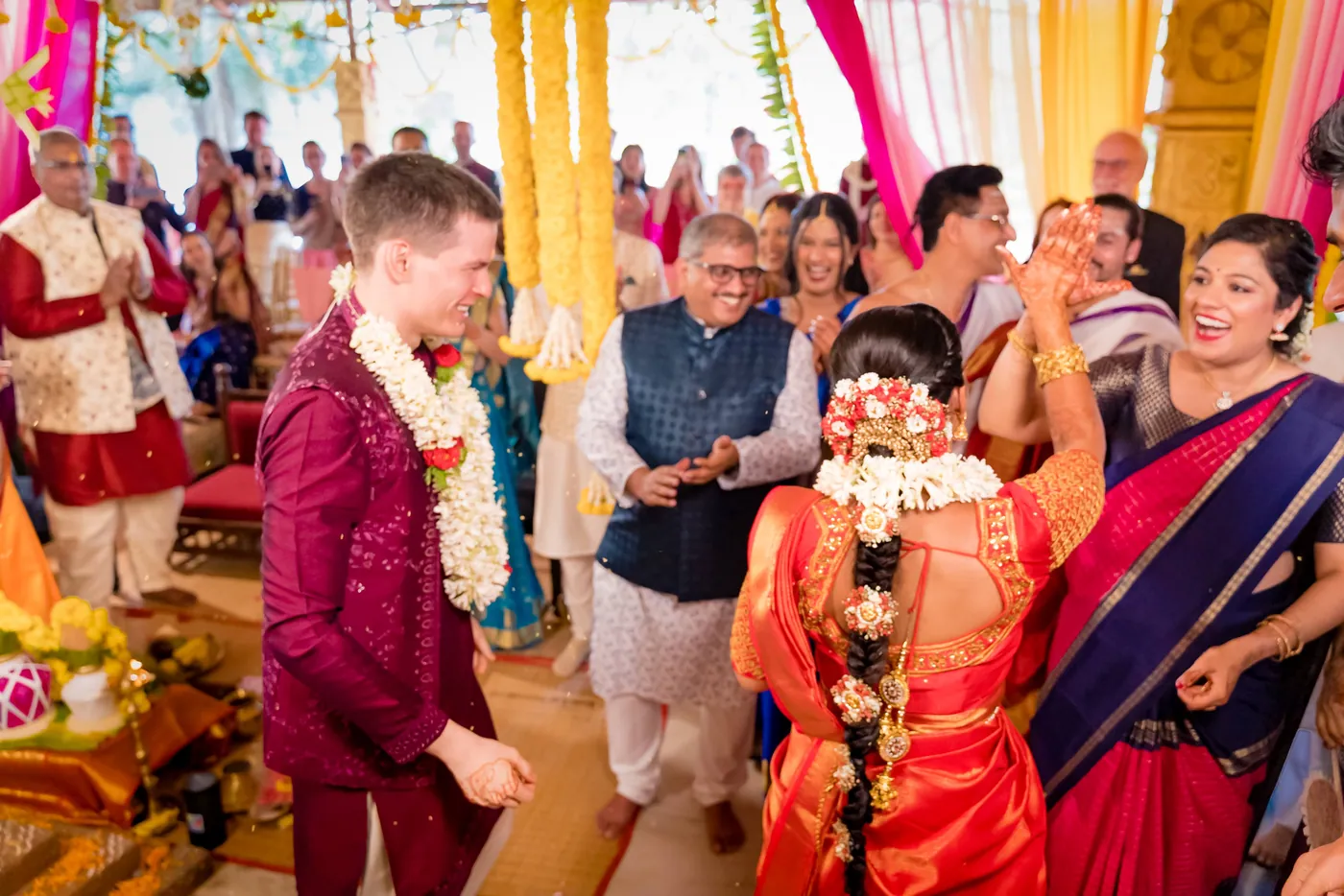 Stefan and Medha stand garlanded among joyful family and a man in a blue vest
