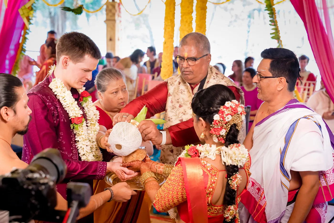 Stefan and Medha sit surrounded by family and priests during a ritual with a coconut