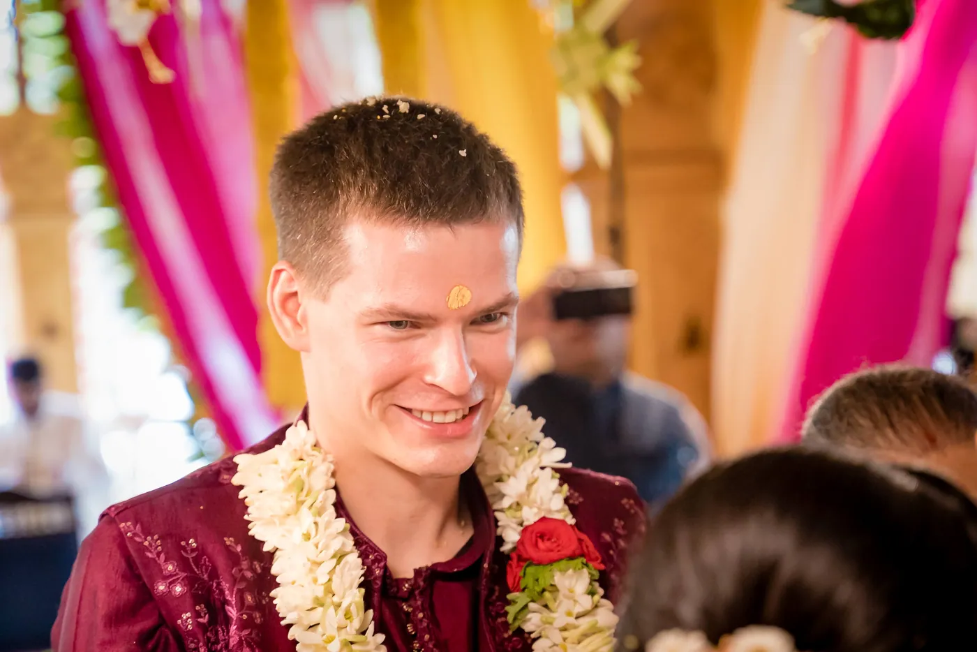 Stefan smiles broadly wearing a jasmine garland with grains of rice on his hair
