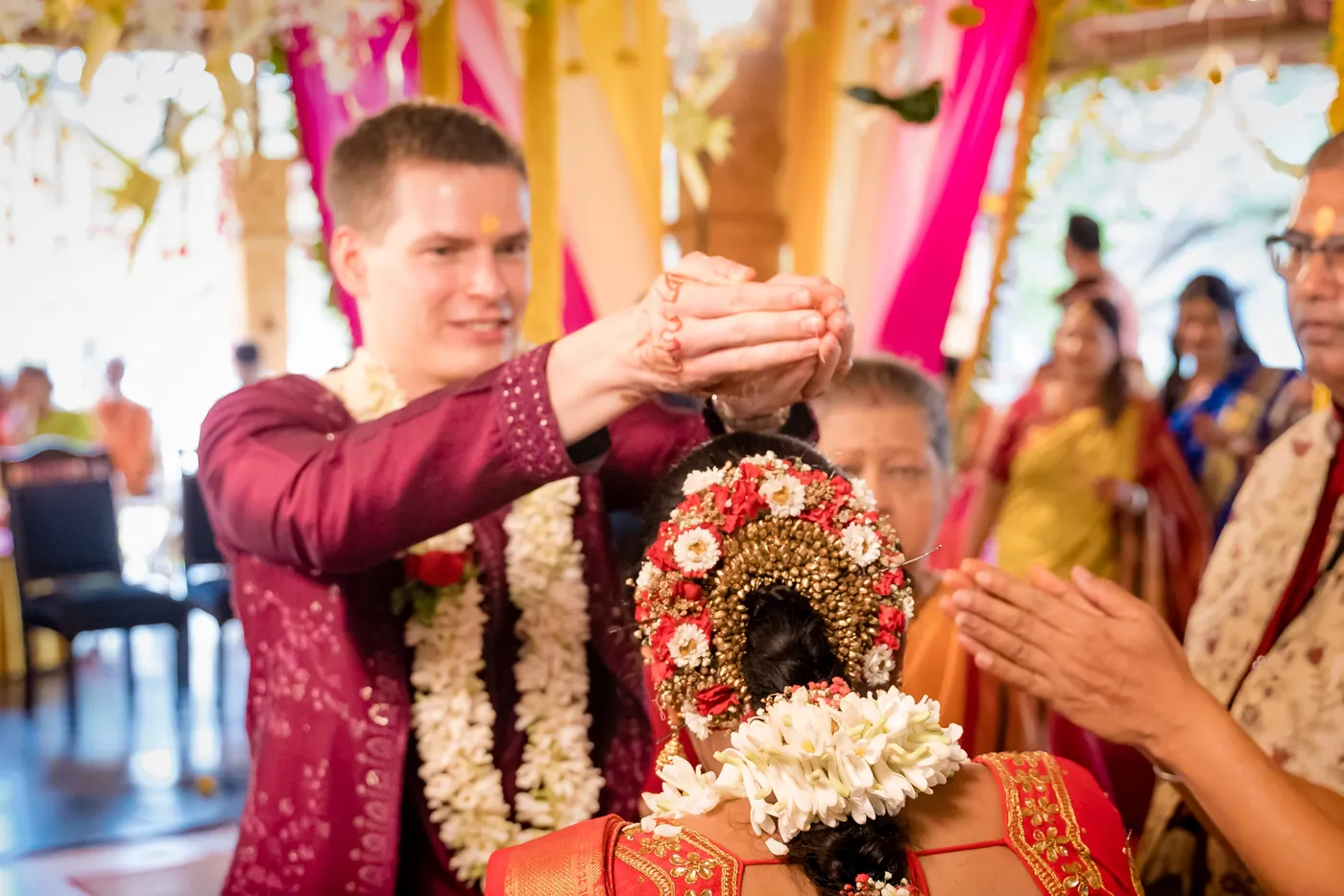 Stefan reaches over Medha with a gesture of blessing while guests look on