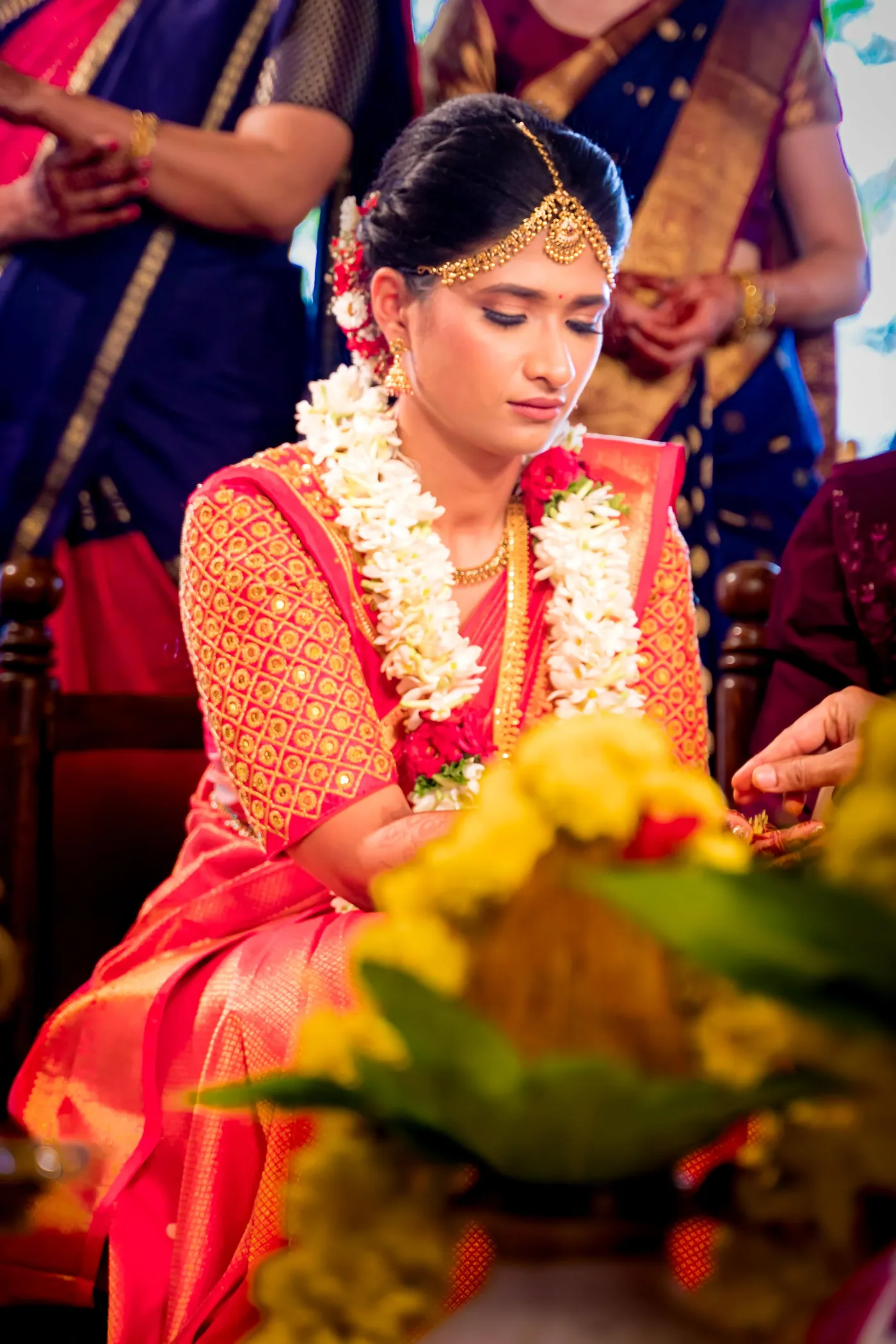 Medha in orange looks down in thought wearing jasmine garlands and a nose ring