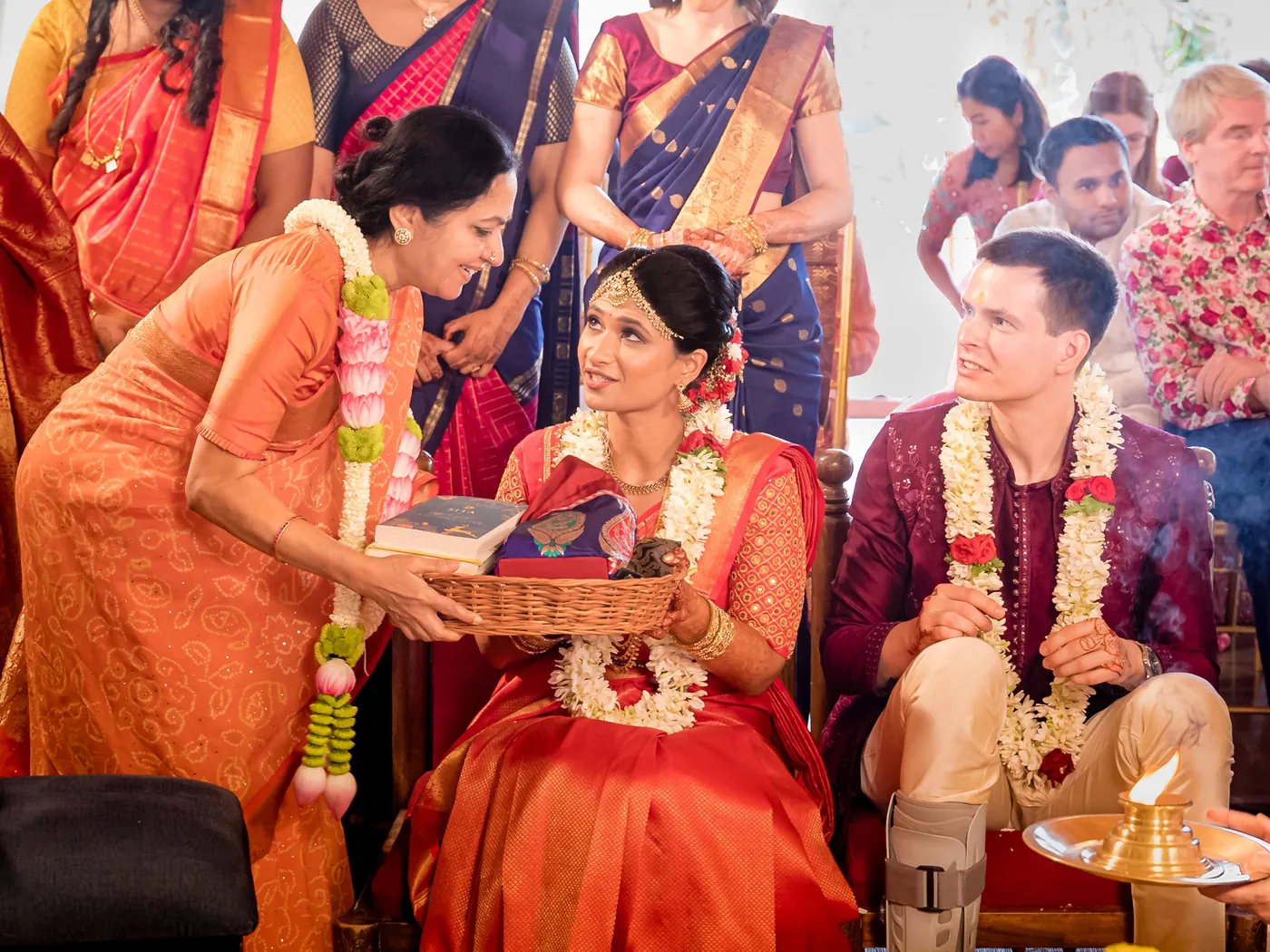 A woman presents a decorated tray to Medha and Stefan as they sit smiling