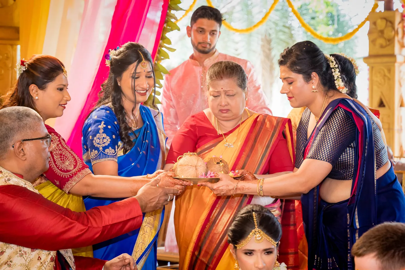A man in red hands a coconut to women in saris during the ritual