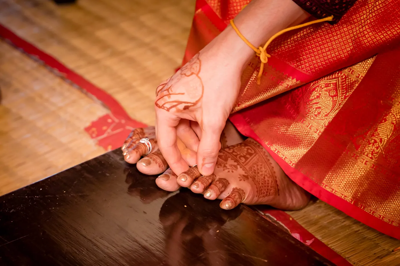 A hand holds Medha's foot beside her red silk sari and a toe ring