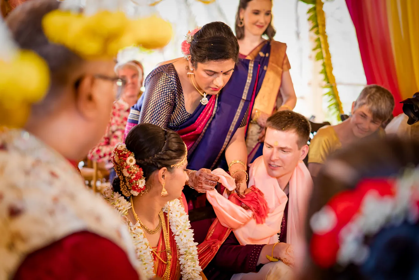A woman in cream and a man in a red waistcoat bend toward Medha and Stefan