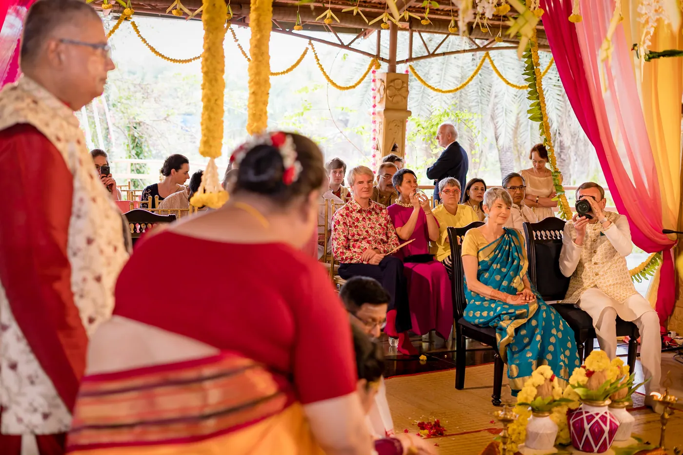 A woman in a red blouse bends in front of seated guests, with the couple behind