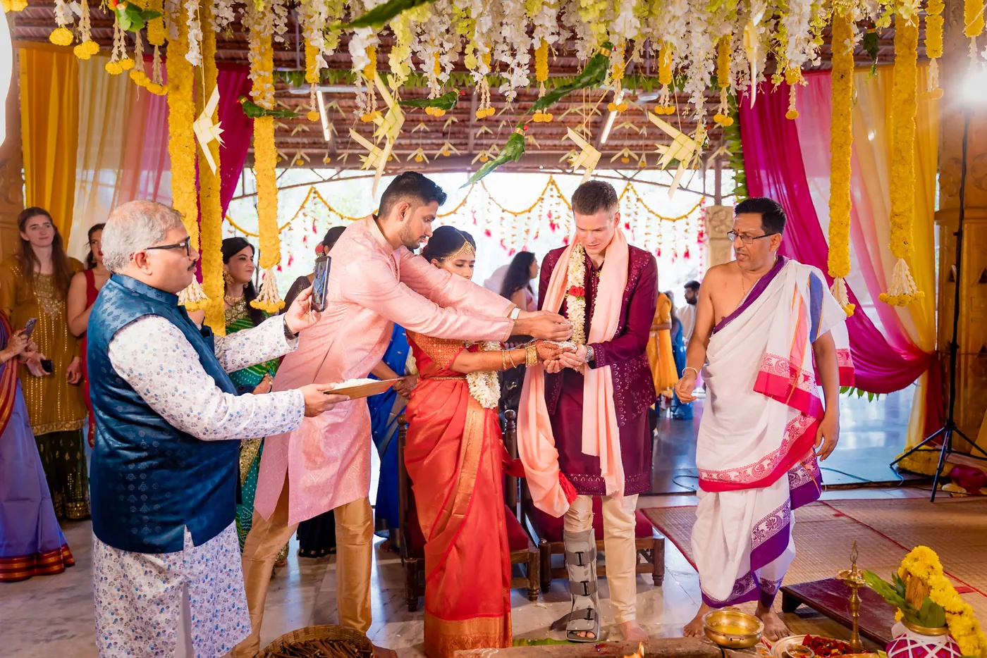 Medha and Stefan stand with elders and a priest in front of the sacred fire