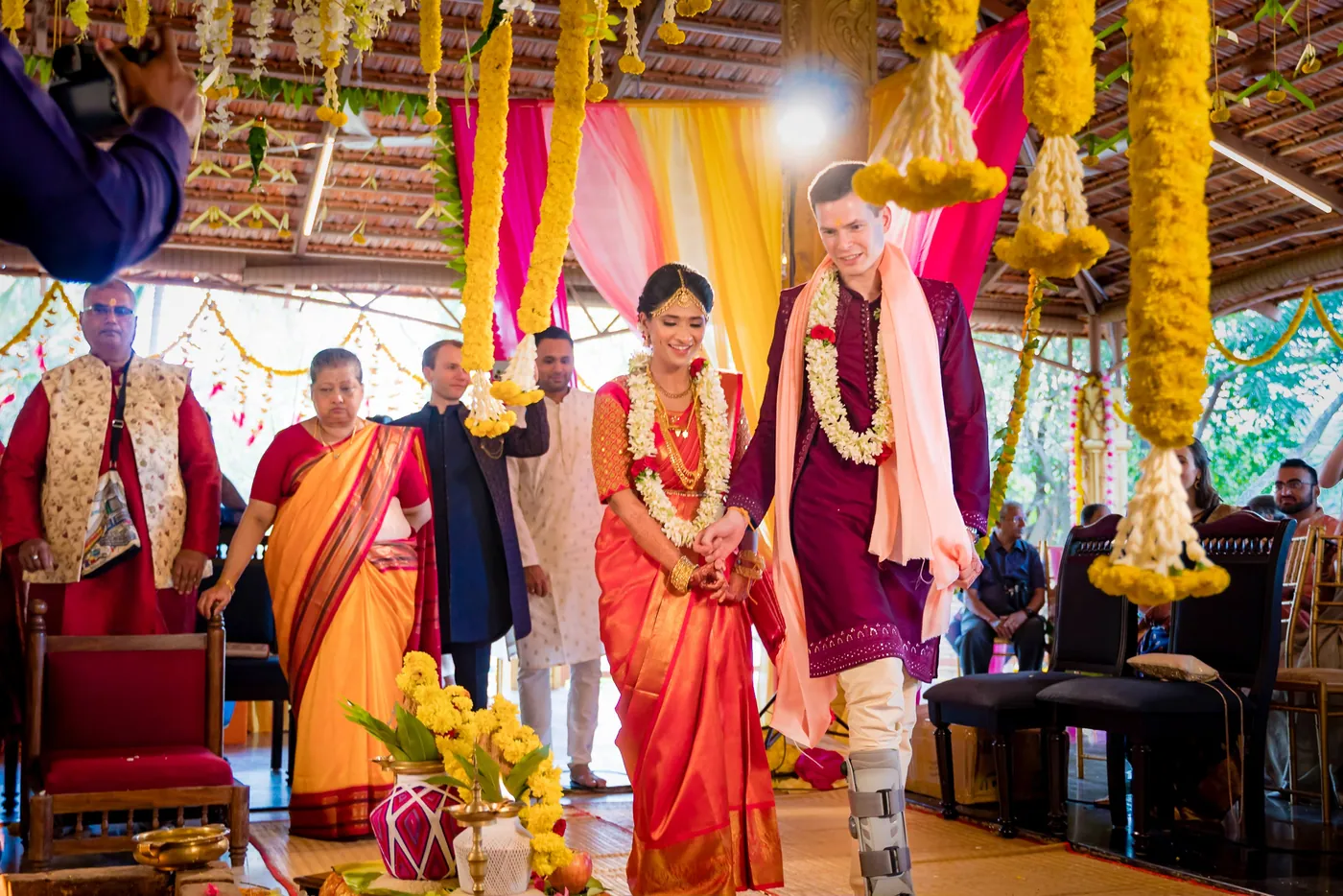 Medha and Stefan walk together toward the fire as guests stand behind them