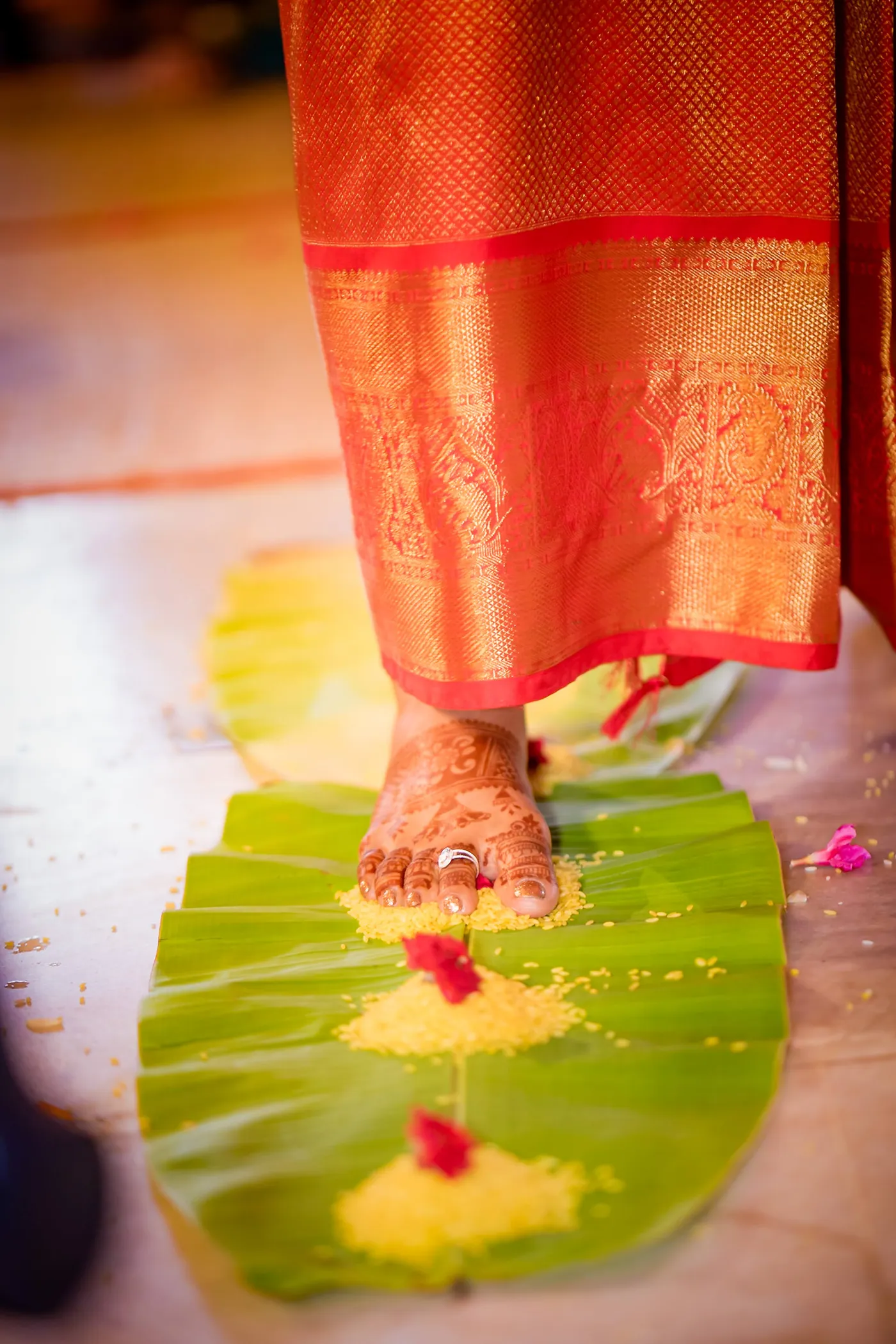 Medha's foot in an orange silk sari rests on a banana leaf with turmeric and red flowers