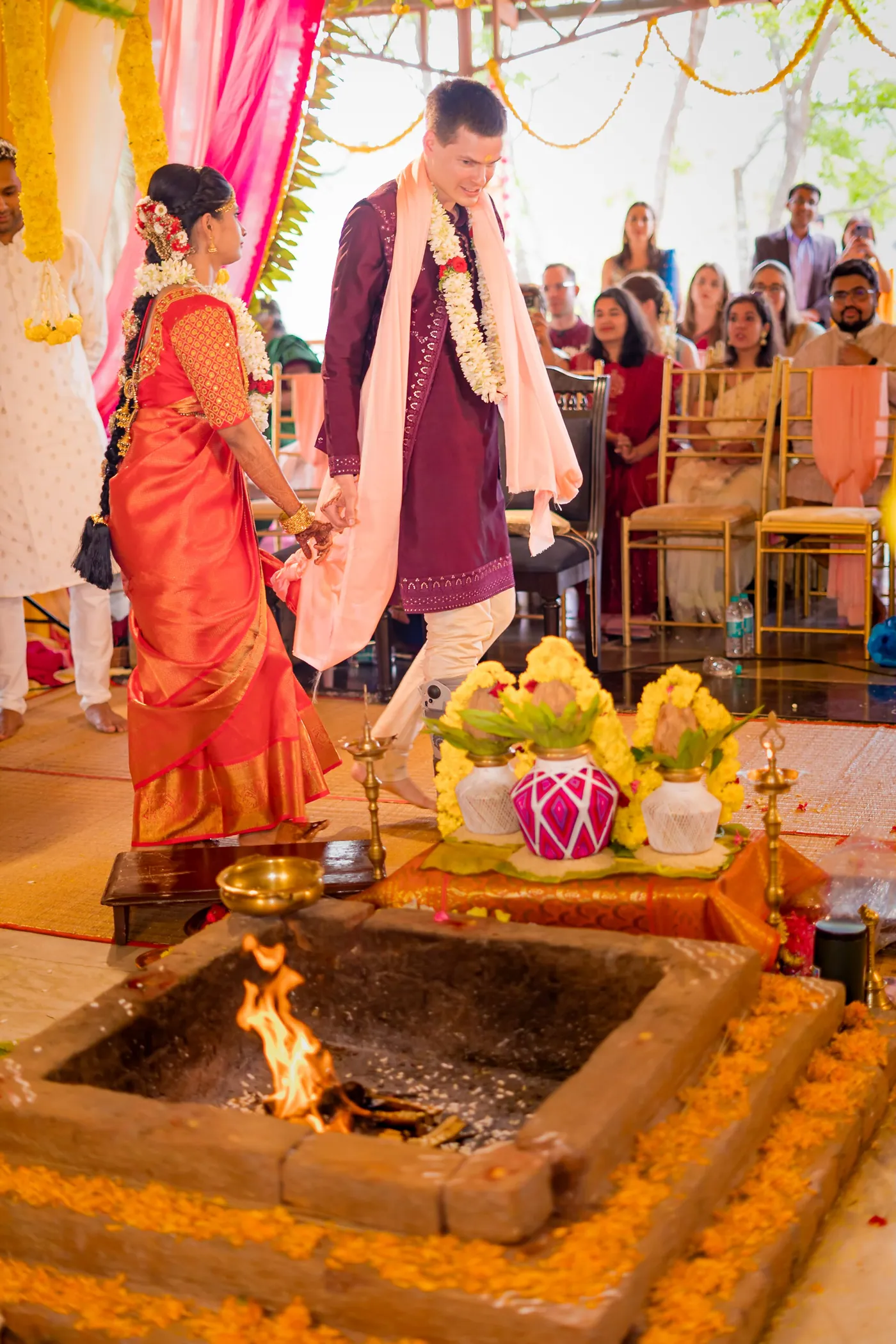 Medha and Stefan walk around a lit sacred fire while guests watch from rows behind