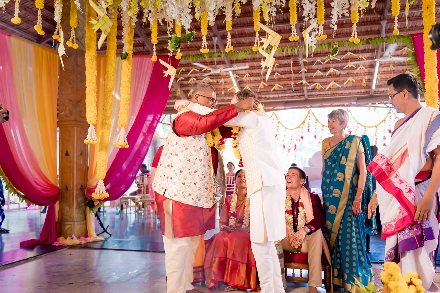 A man in cream and Stefan stand with Medha under pink drapes at the ceremony hall