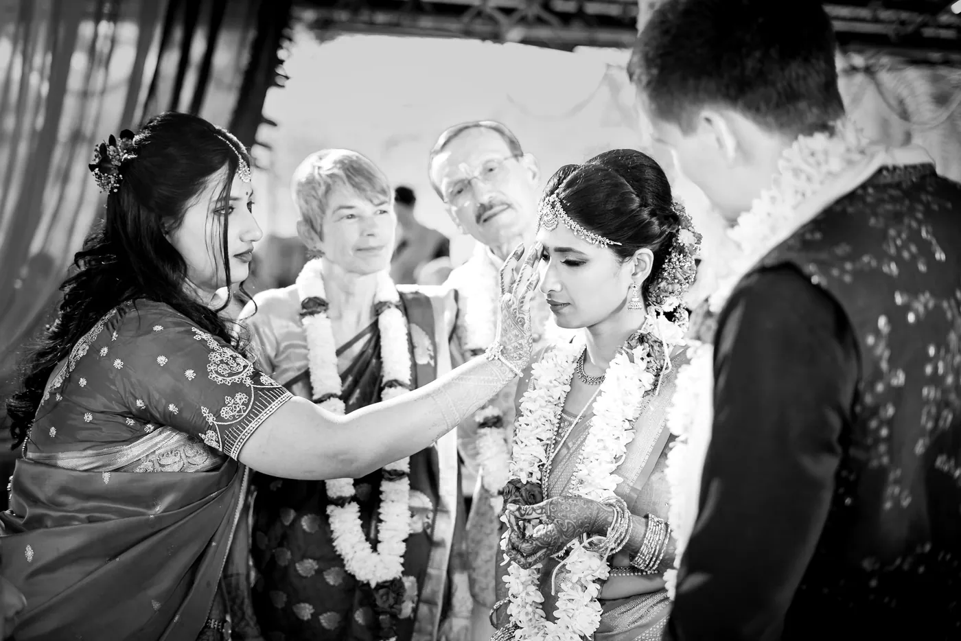 Black and white of a woman placing a garland on Medha as Stefan stands in a dark jacket