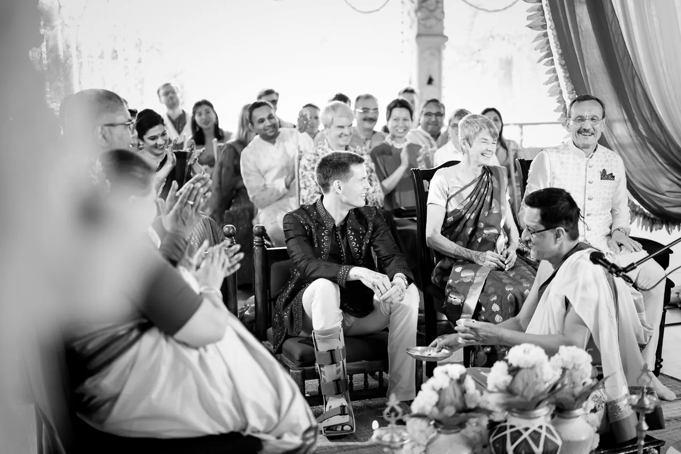 Stefan with a walking boot on one leg grins beside his mother as a priest and guests look on