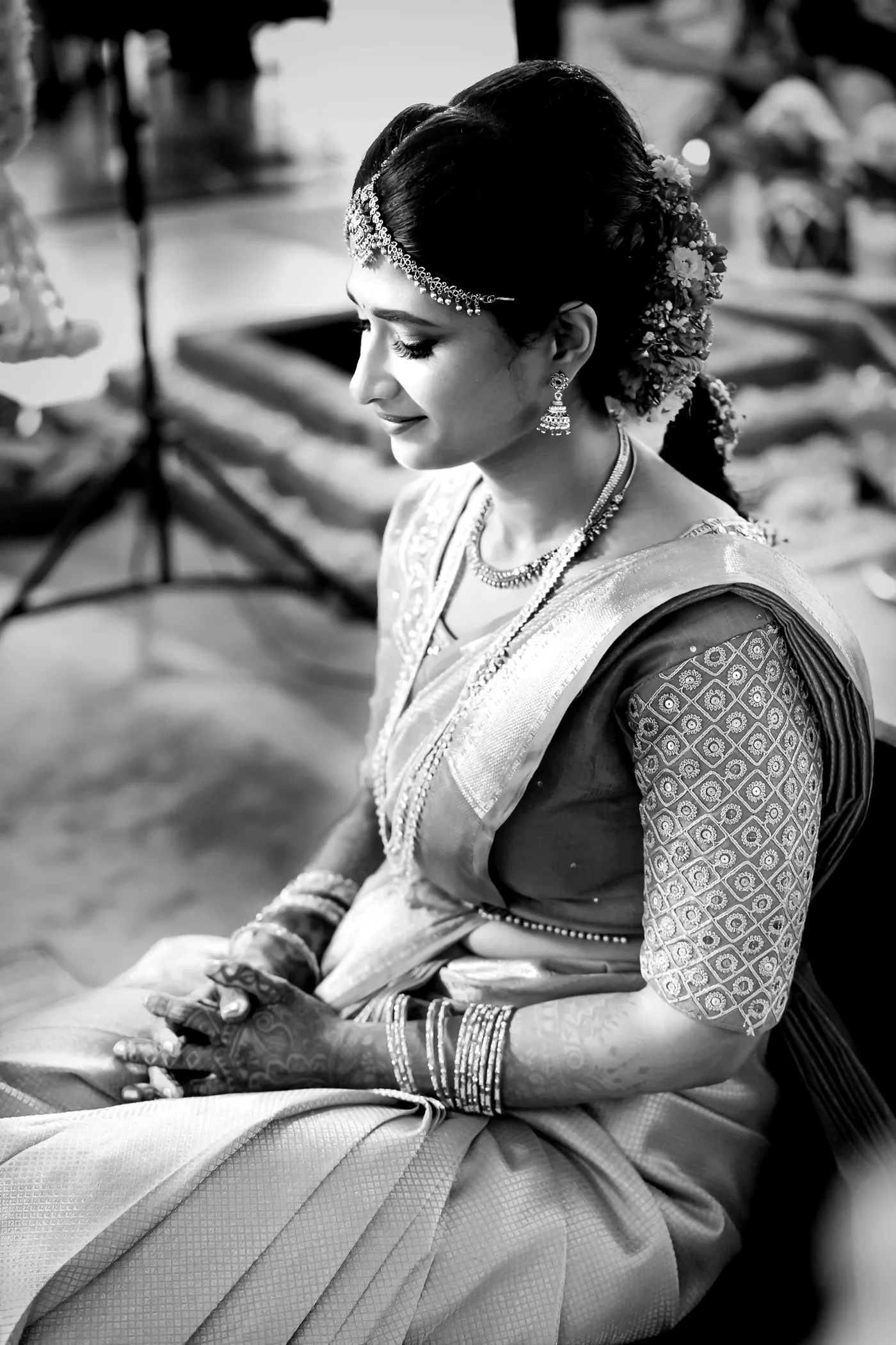 Black and white of Medha seated on the floor looking down, her bangles and sari folds in the frame