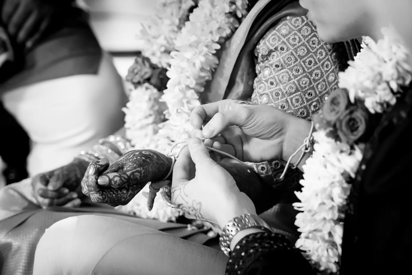 Black and white of henna decorated hands holding jasmine garlands, bangles at the wrist