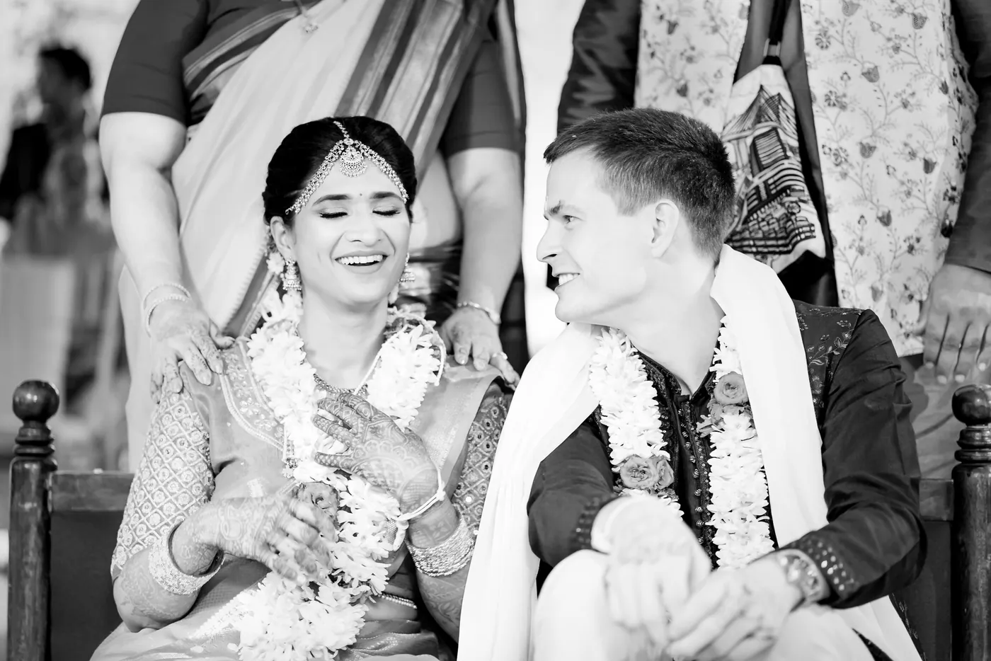 Black and white of Medha laughing with delight beside Stefan while a hand rests on her shoulder