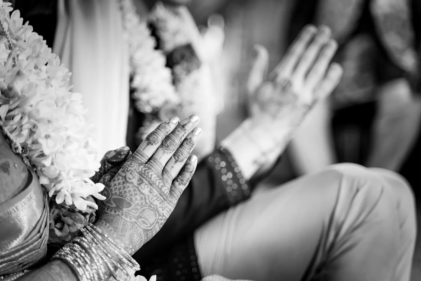 Black and white of henna decorated hands pressed together over white jasmine garlands
