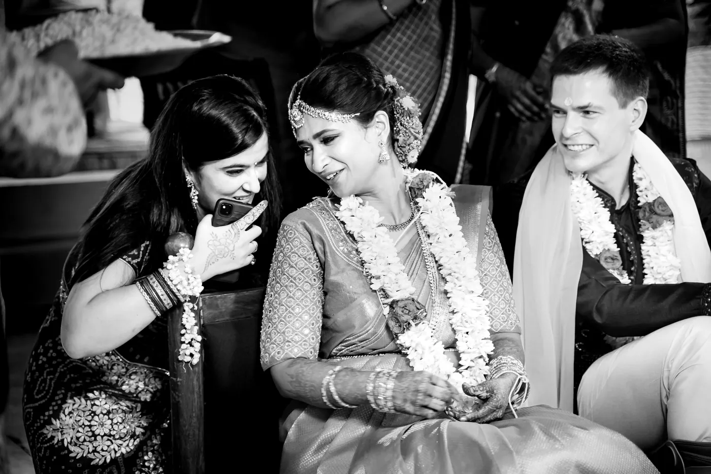 Black and white of Medha and a woman beside her laughing while garlanded Stefan sits quietly