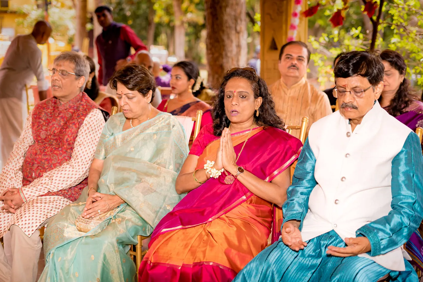 Five seated guests in colorful silks watch the ceremony, two with folded hands