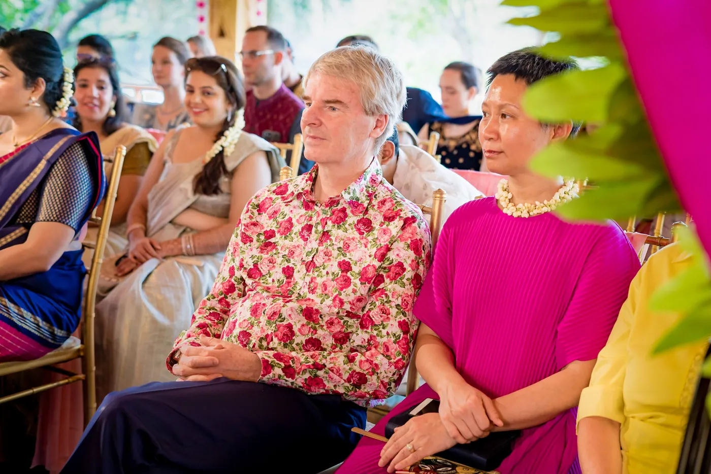 Guests seated in rows watch the ceremony, among them a man in a floral shirt
