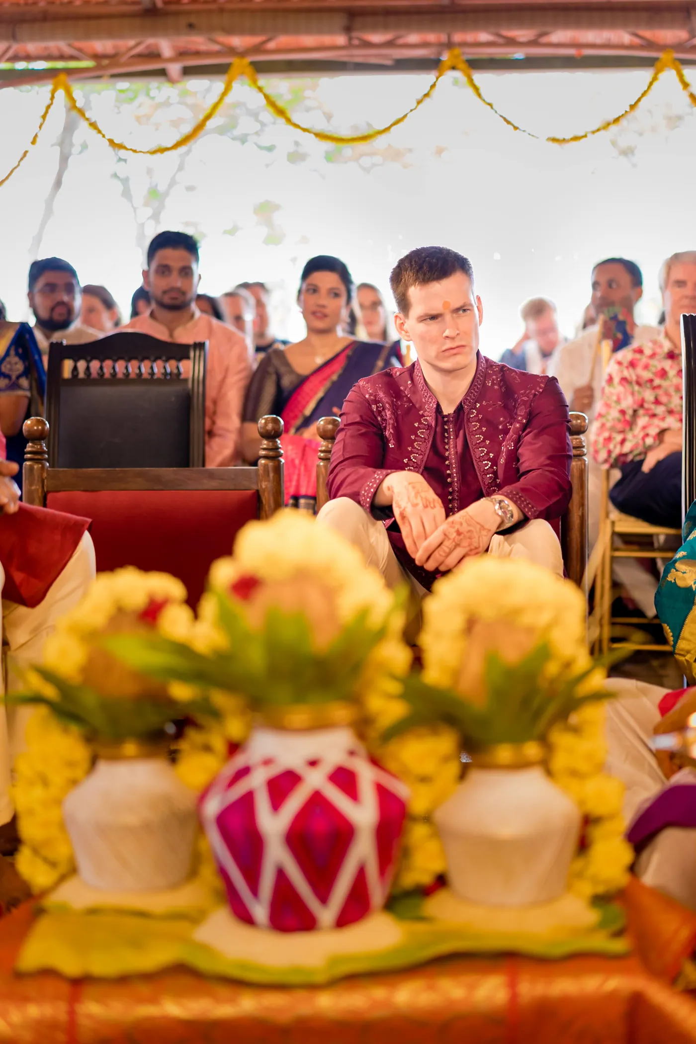 Stefan sits among guests behind ceremonial pots decorated with yellow flowers and mango leaves