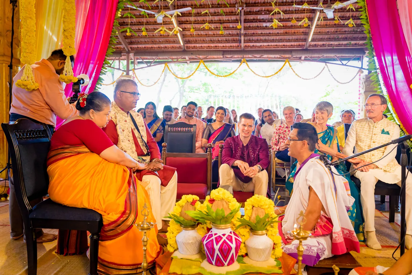Guests watch from their chairs as a family sits near the pots of the ceremony