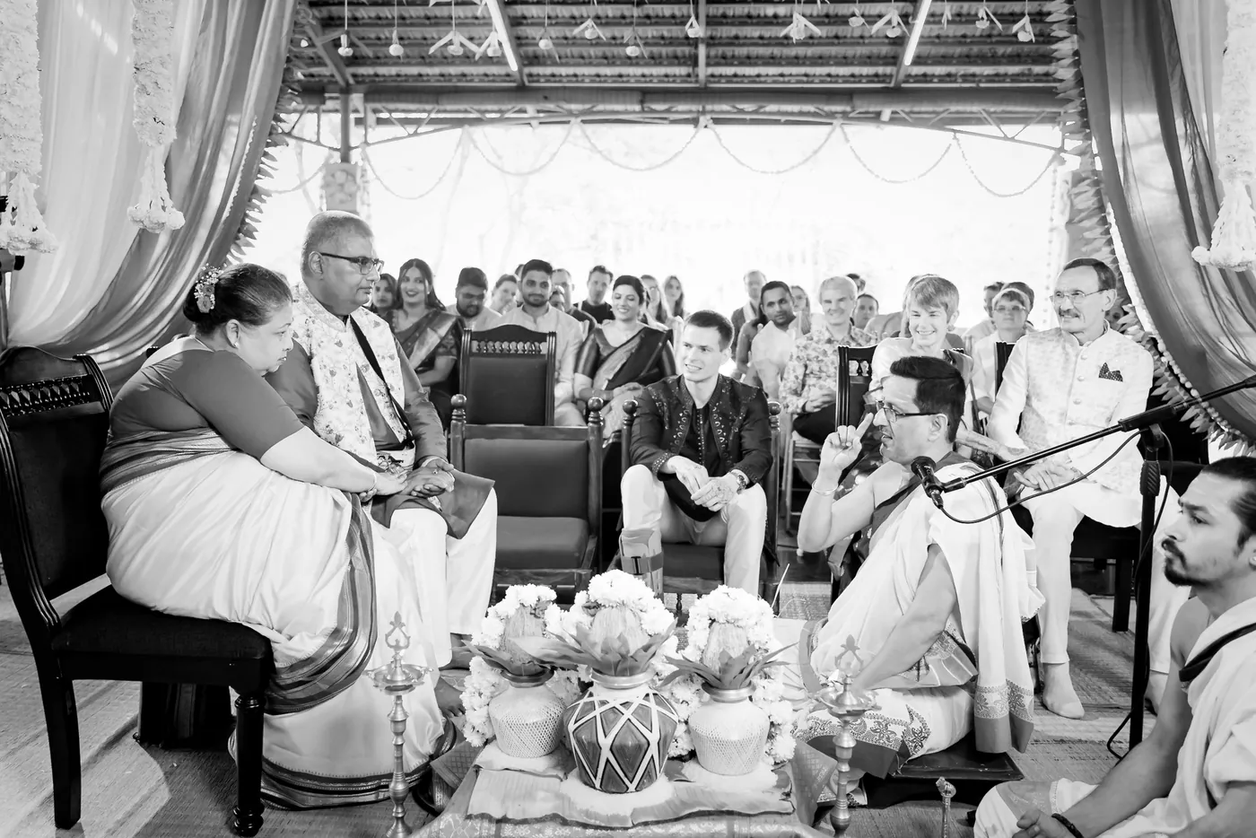 Black and white of the ceremony hall with seated guests and priests around decorated pots