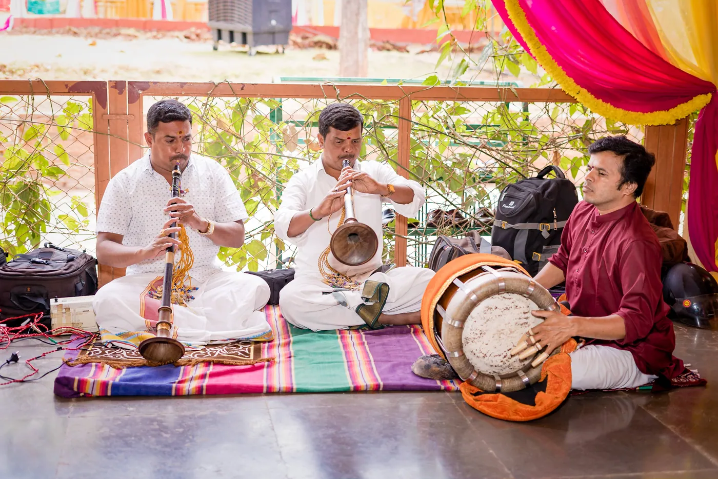 Three musicians play wind and drum instruments on a striped mat during the ceremony