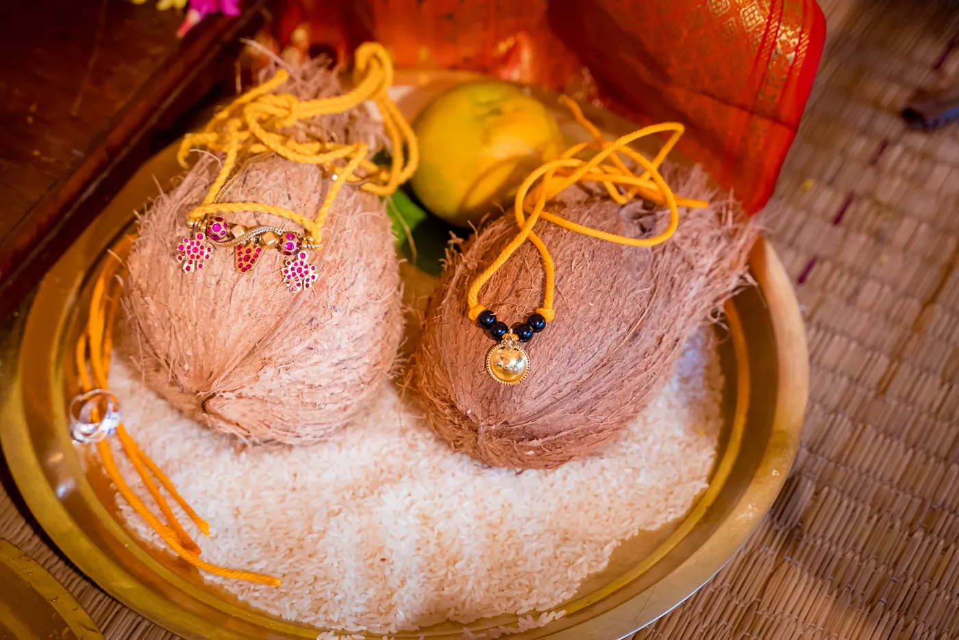 Two coconuts with sacred threads rest on a bed of rice in a brass tray