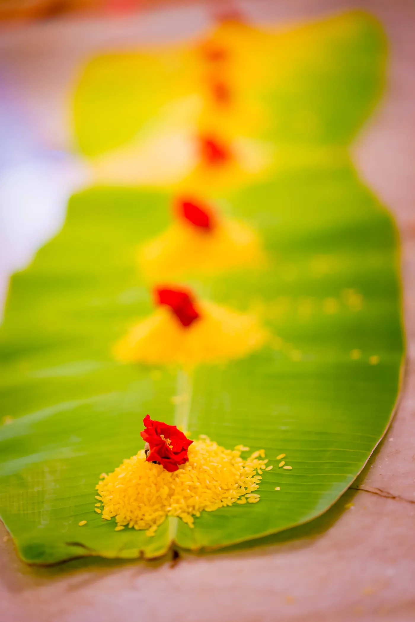 A banana leaf with a line of red flowers and turmeric lies on the floor